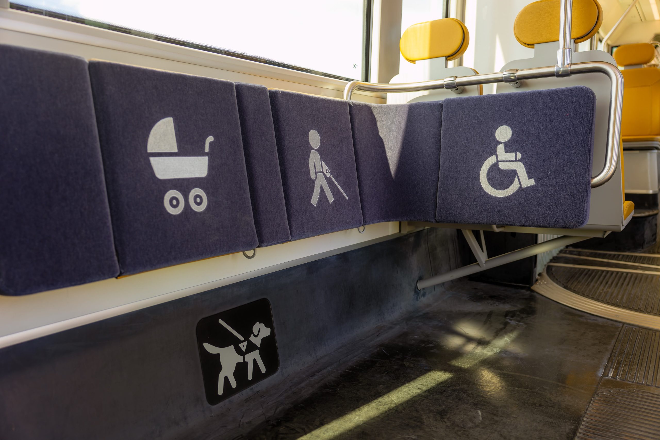 Pyörätuoli-, opaskoira-, valkoinen keppi- ja lastenvaunusymbolein merkityt istuimet vaunussa.